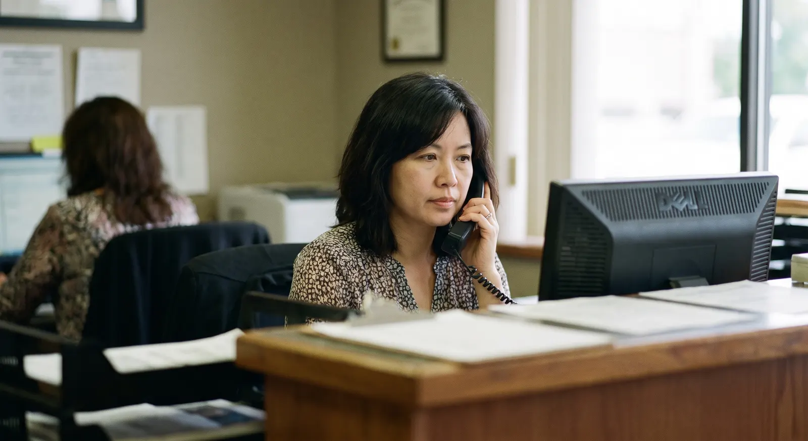 Medical receptionist answering a patient call at the front desk — Rinqly's AI medical answering service picks up 24/7 when the desk is busy